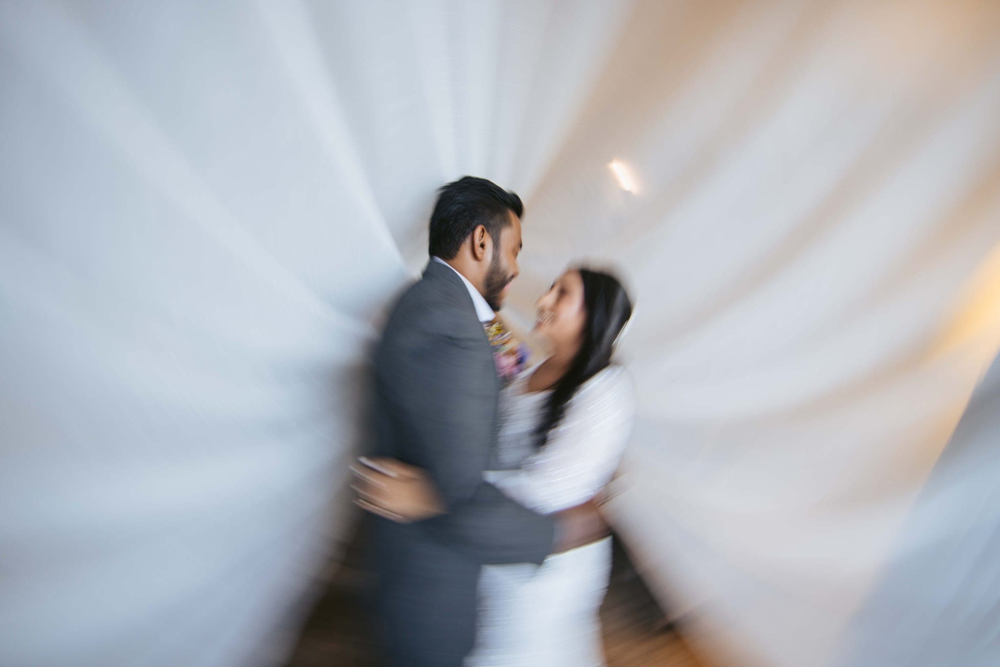 Blurred motion of couple embracing behind sheer white drapes