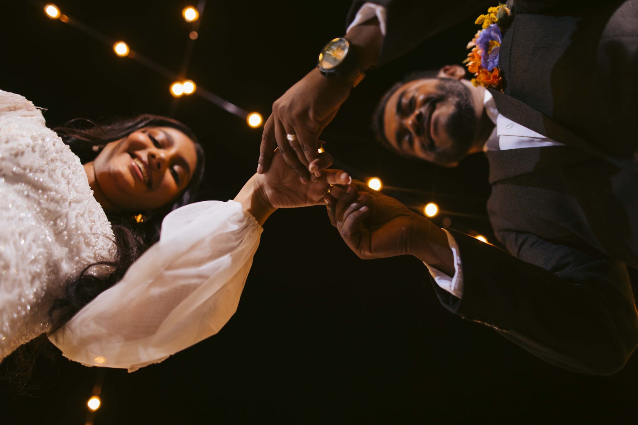 Couple joining hands under string lights at reception