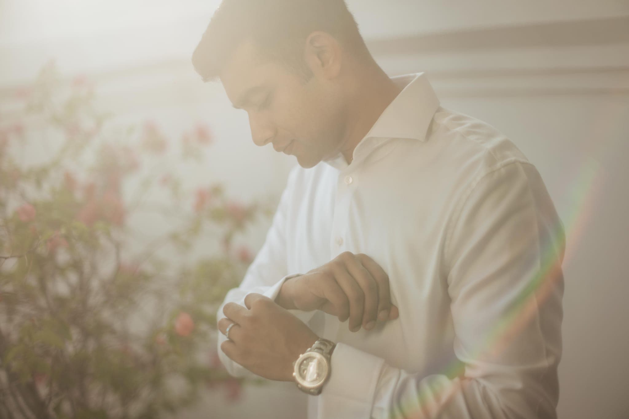 Groom fastening cufflink watch in warm hazy light