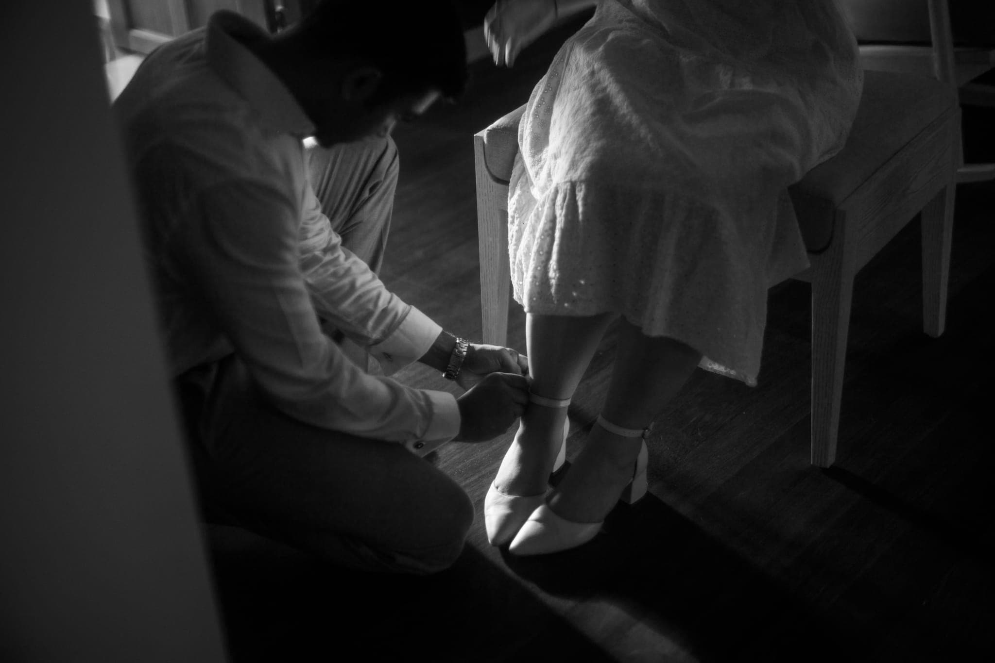 Groom kneeling to fit bride's shoe in dim light