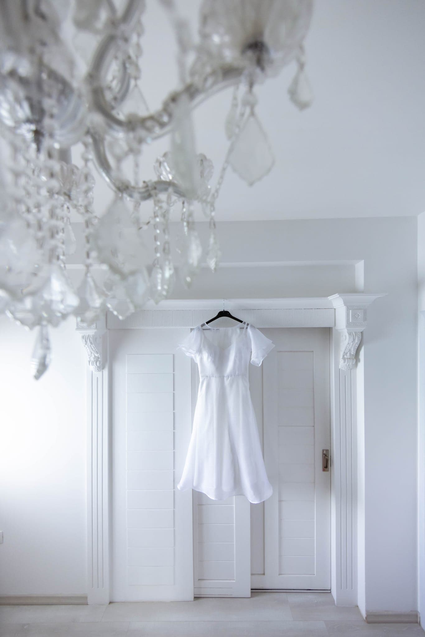 White wedding dress hanging beneath crystal chandelier