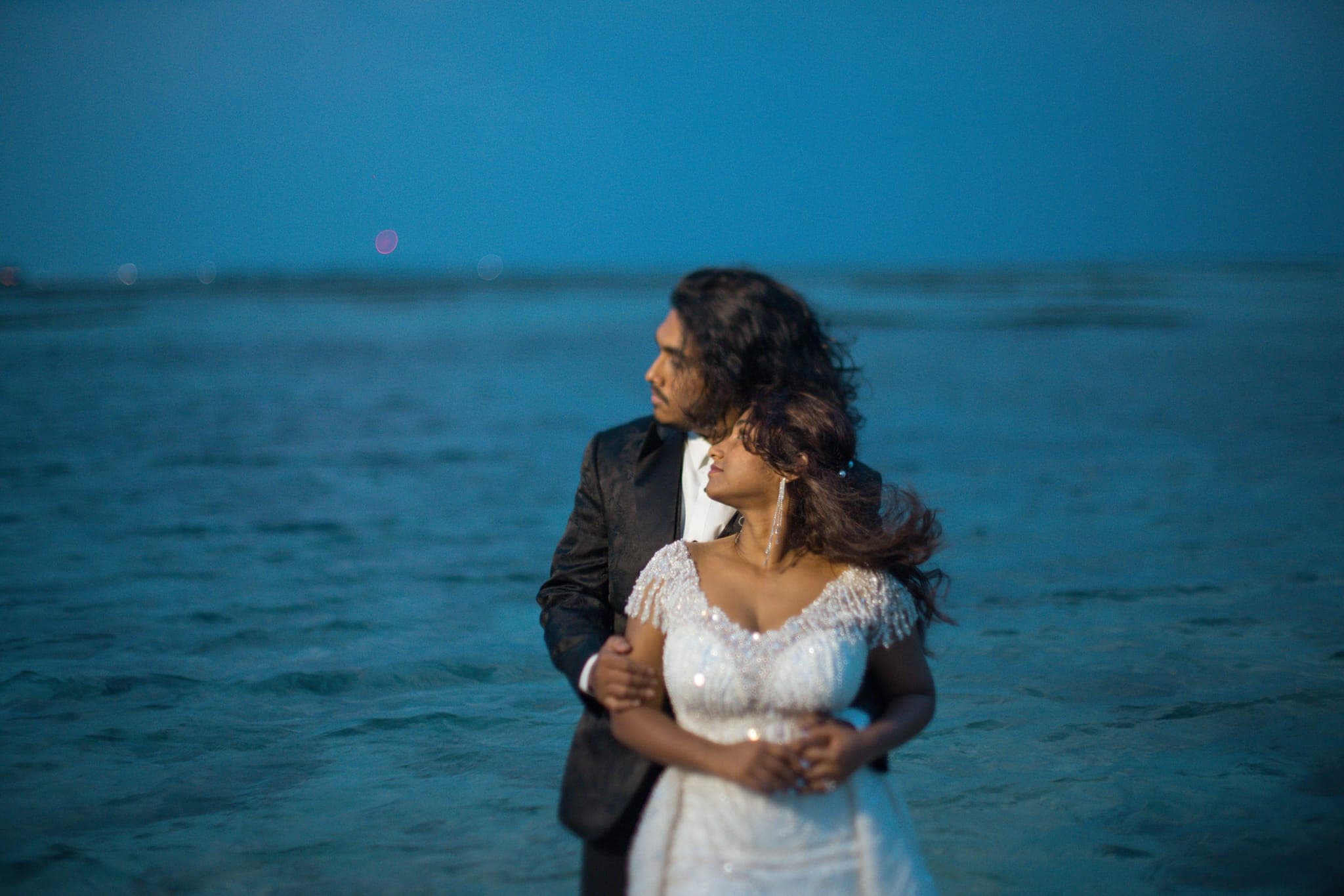 Bride and groom embracing on beach at dusk