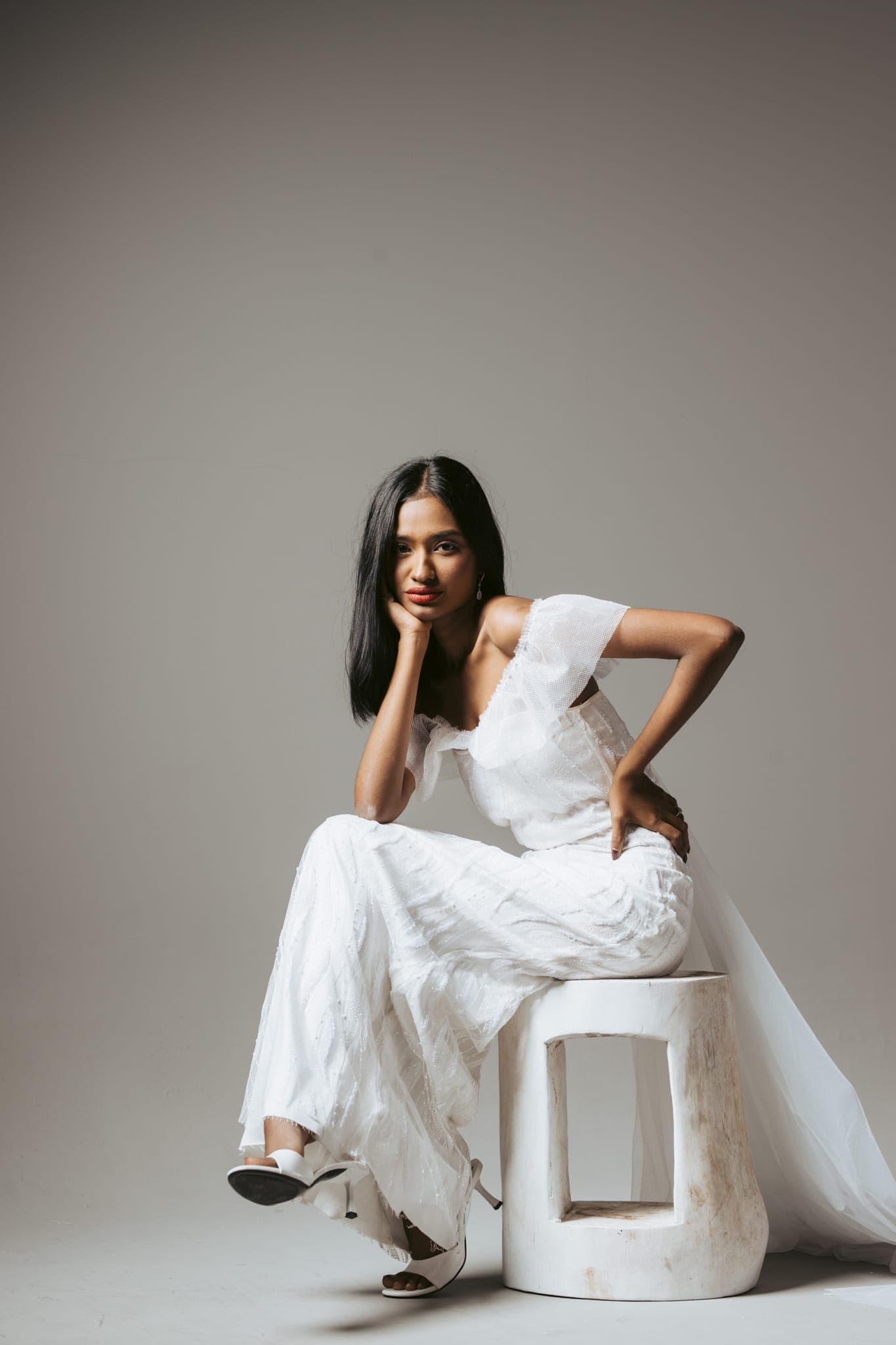 Woman in white gown seated on studio pedestal