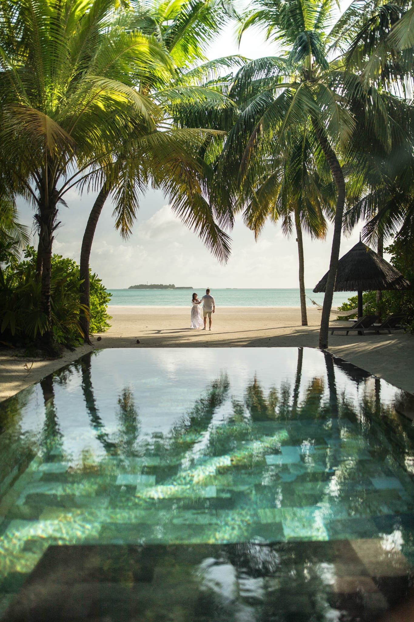 Couple walking beach beside tropical infinity pool