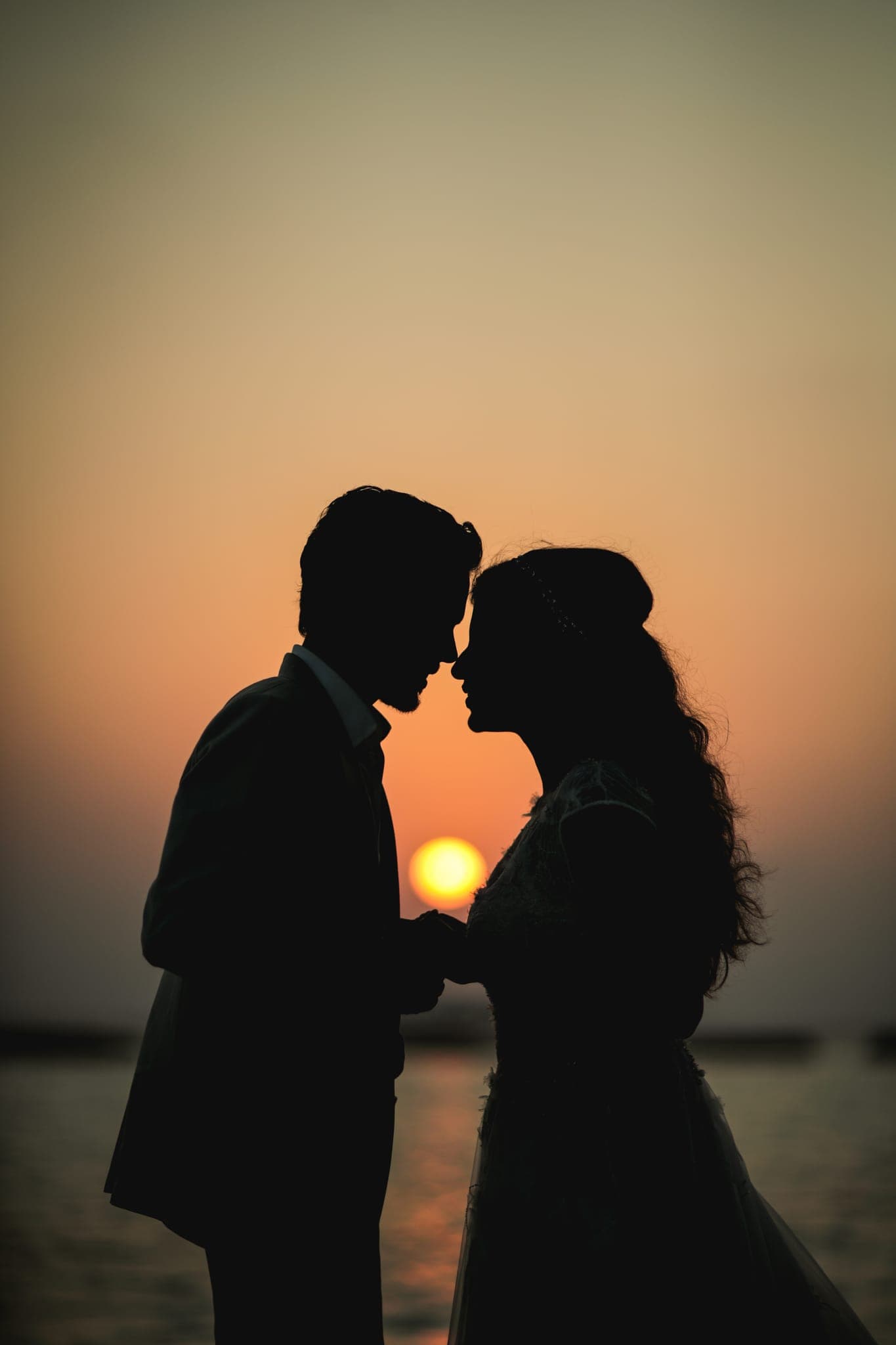 Couple foreheads touching, silhouetted against sunset sun