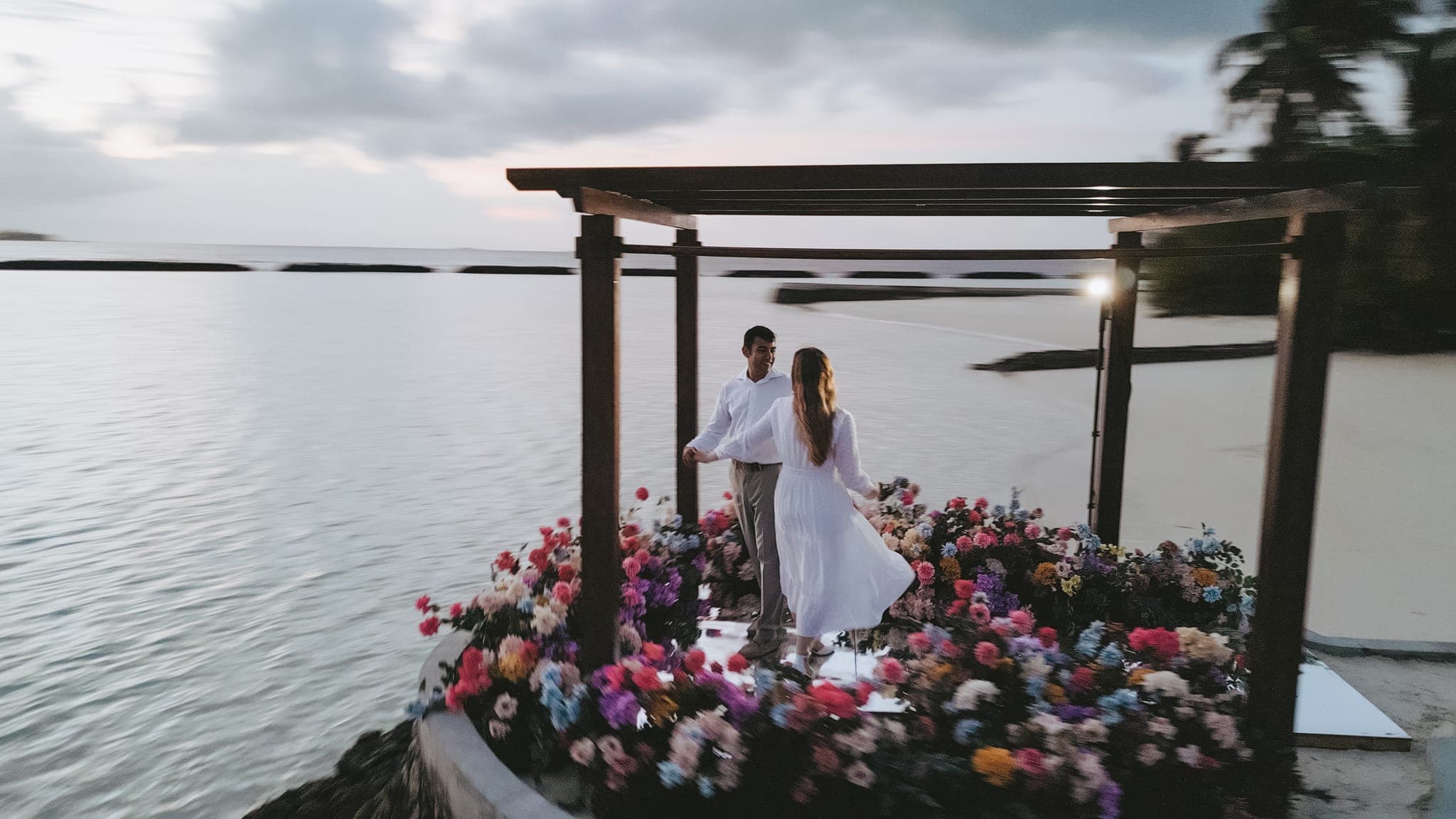 Aerial view of couple at flower-decorated overwater pergola