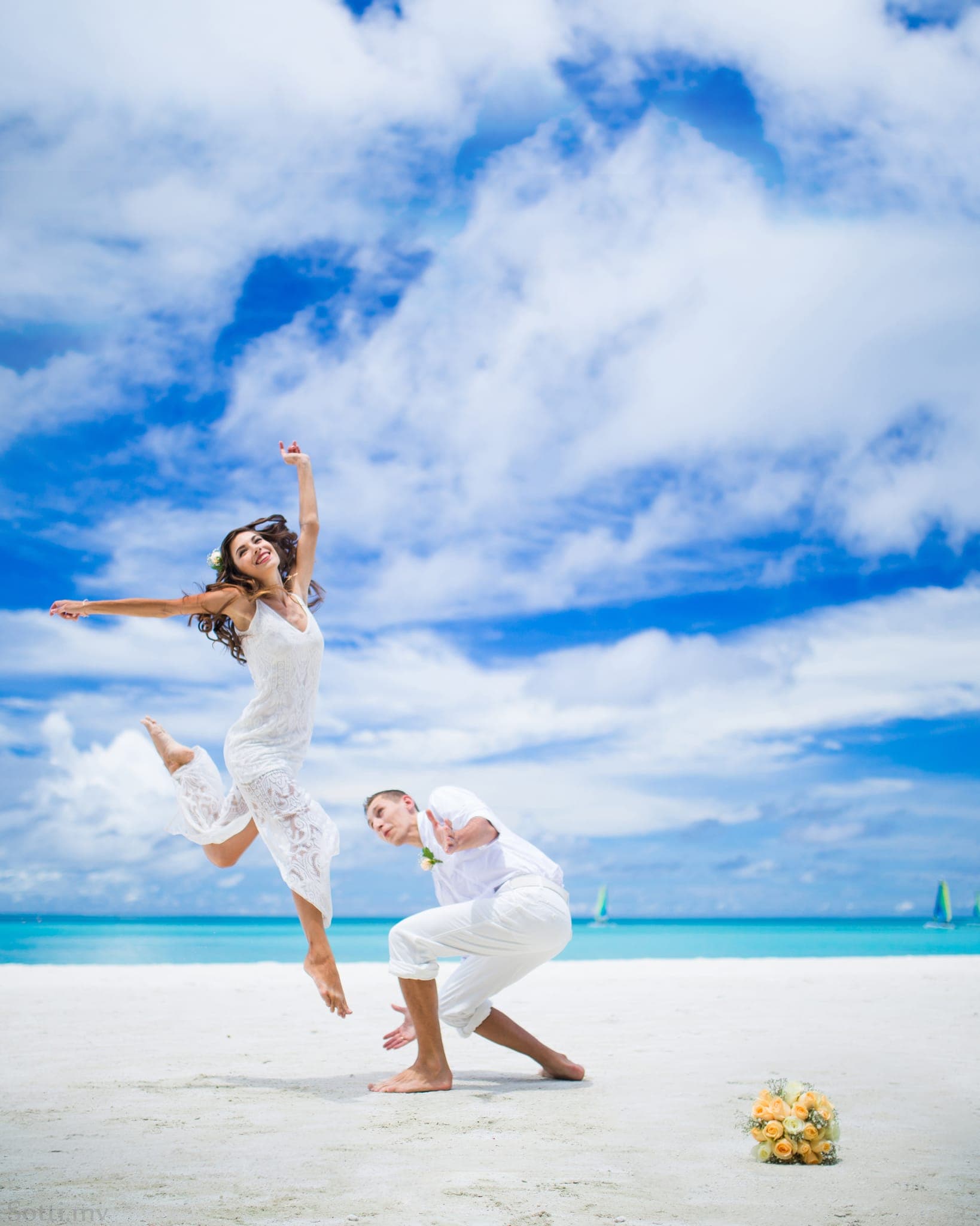 Bride leaping joyfully on beach with groom kneeling