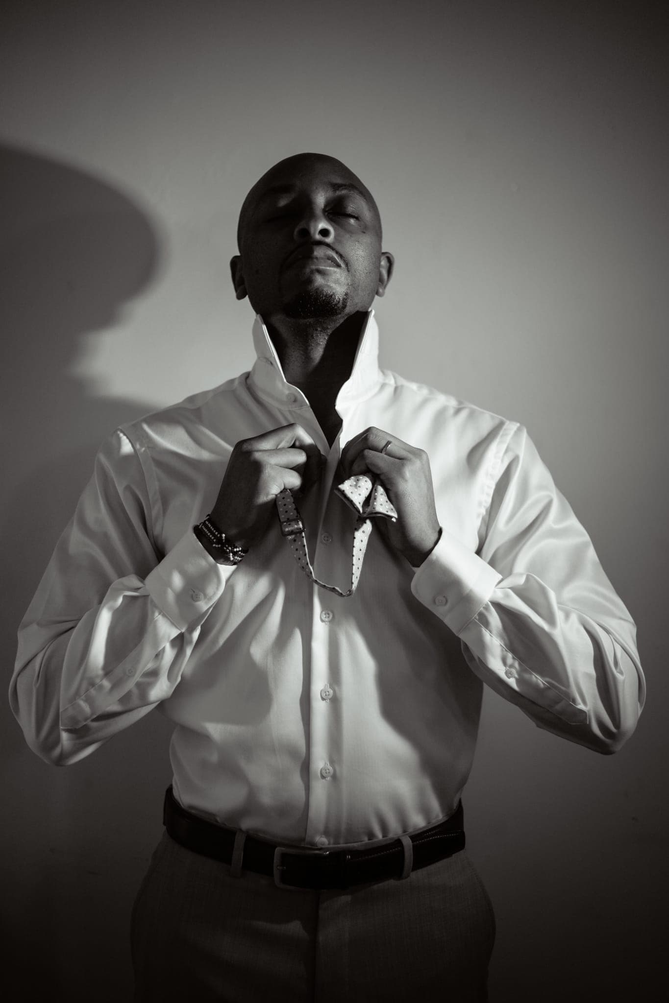 Man in white shirt adjusting collar in dramatic studio light