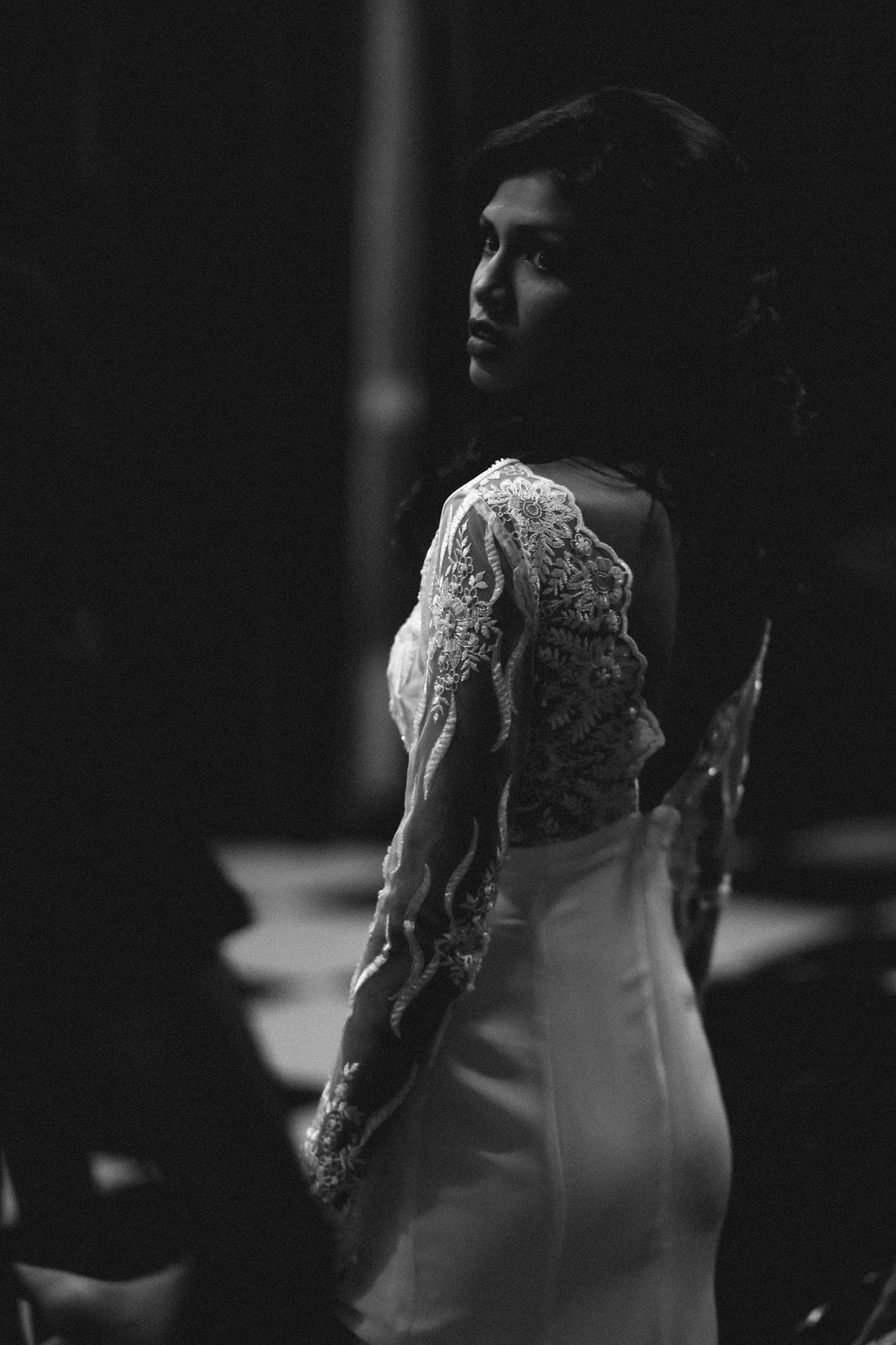 Bride in lace gown looking over shoulder in dark room