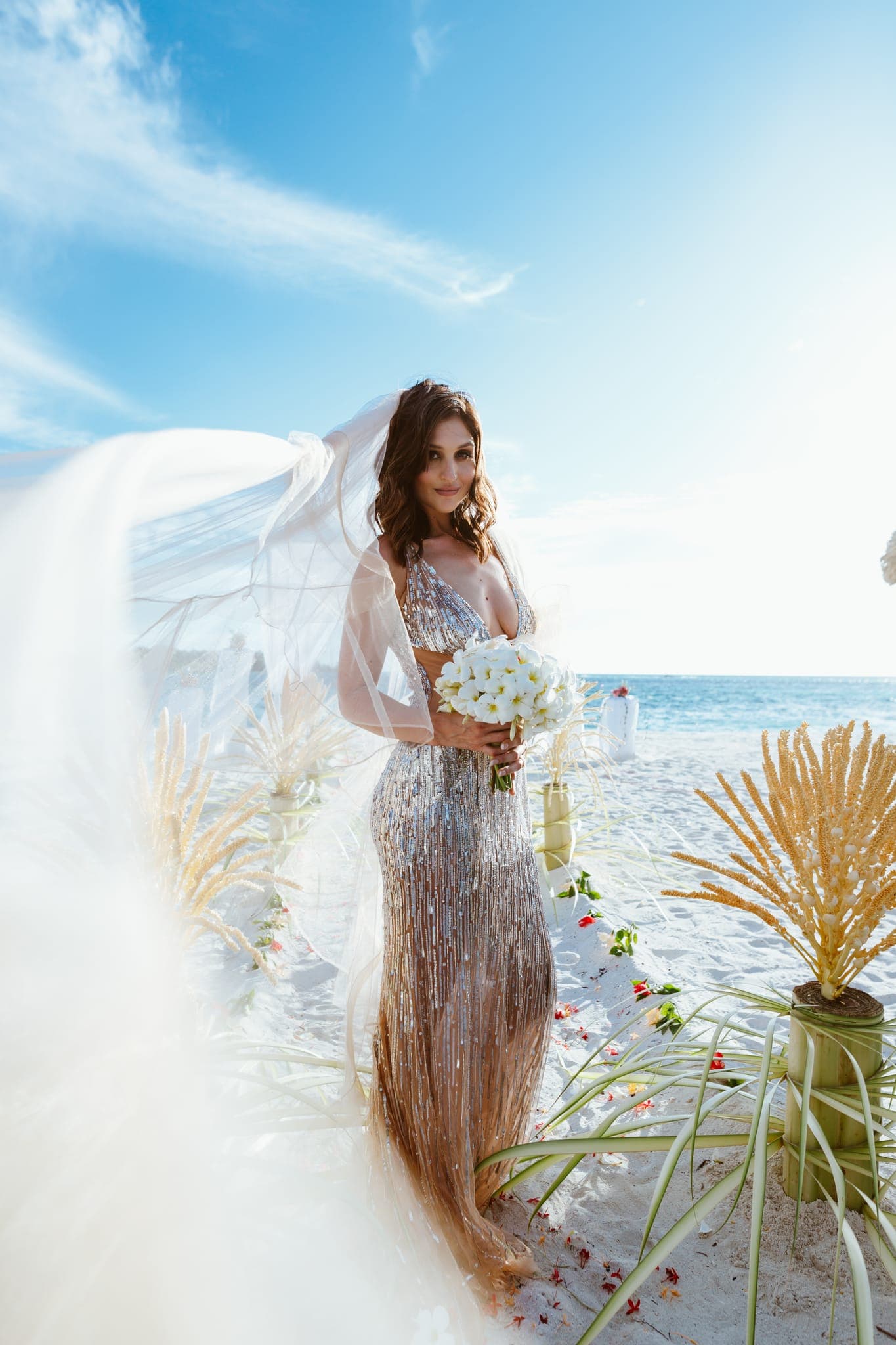 Bride in flowing veil holding bouquet on beach