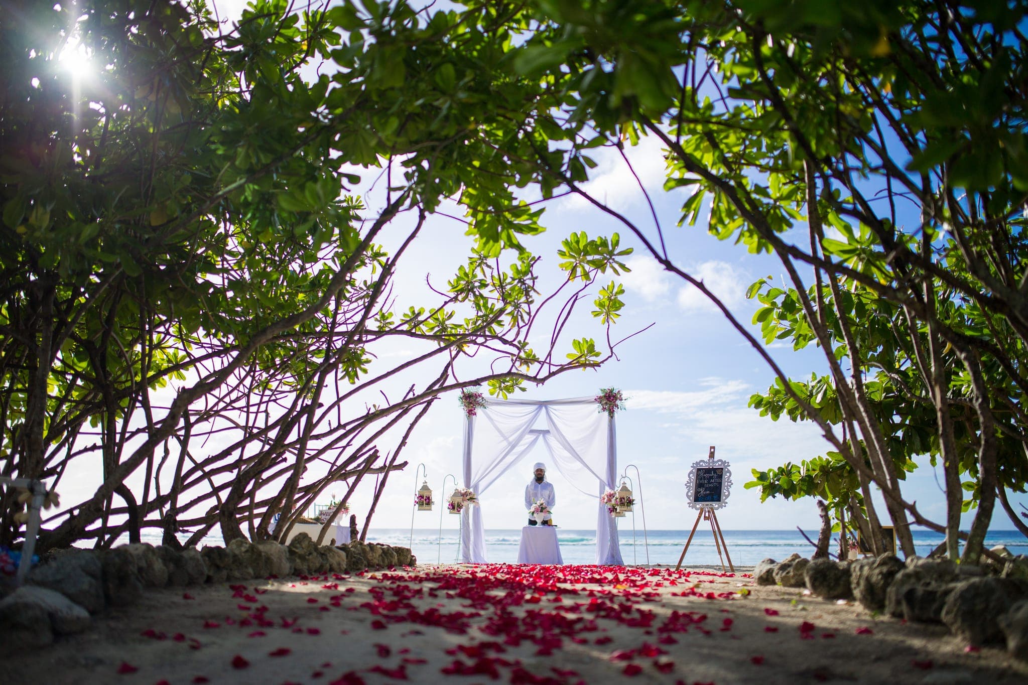Beach wedding arch decorated with red rose petal aisle