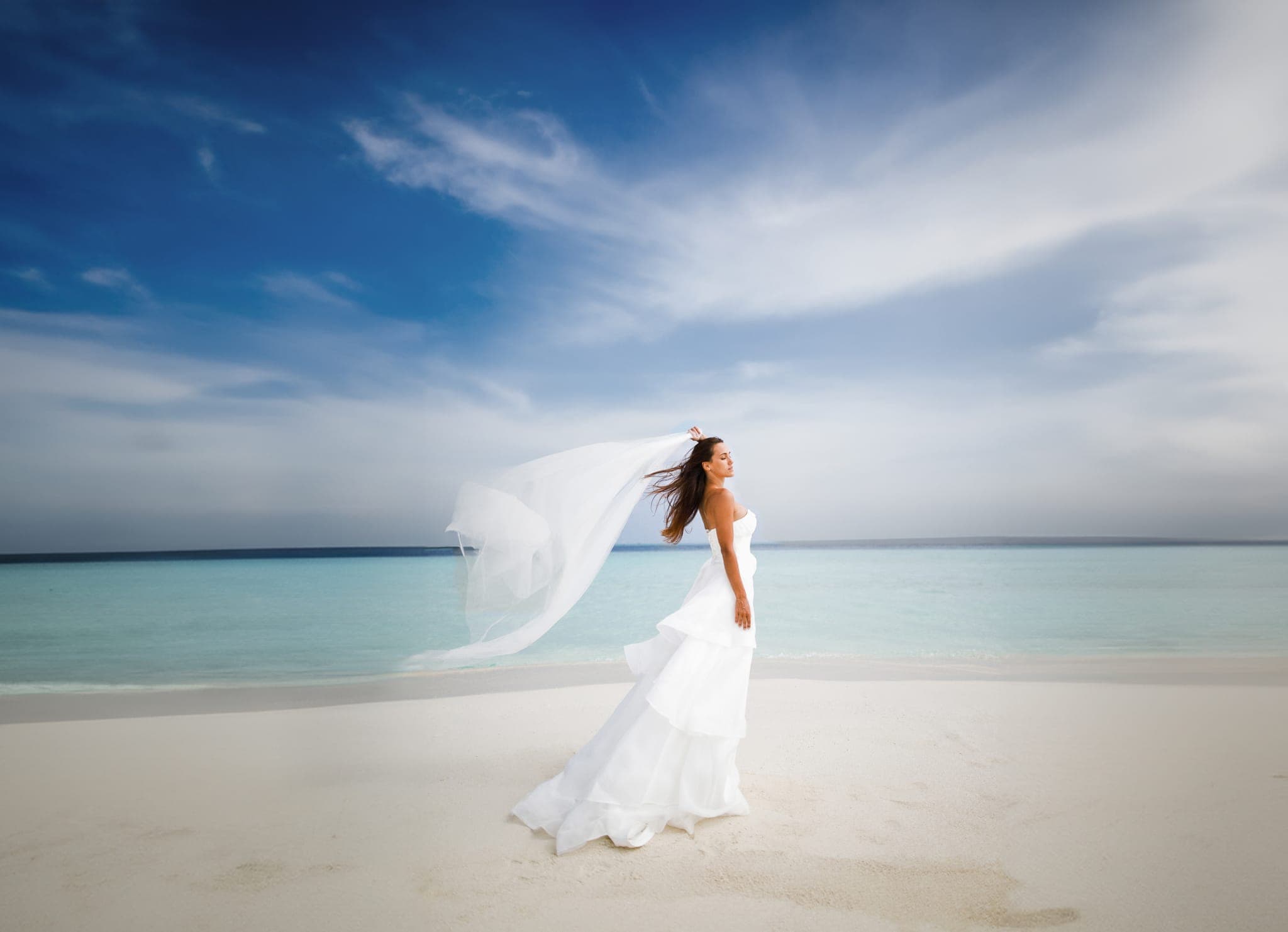 Bride's veil billowing in wind on white sand beach