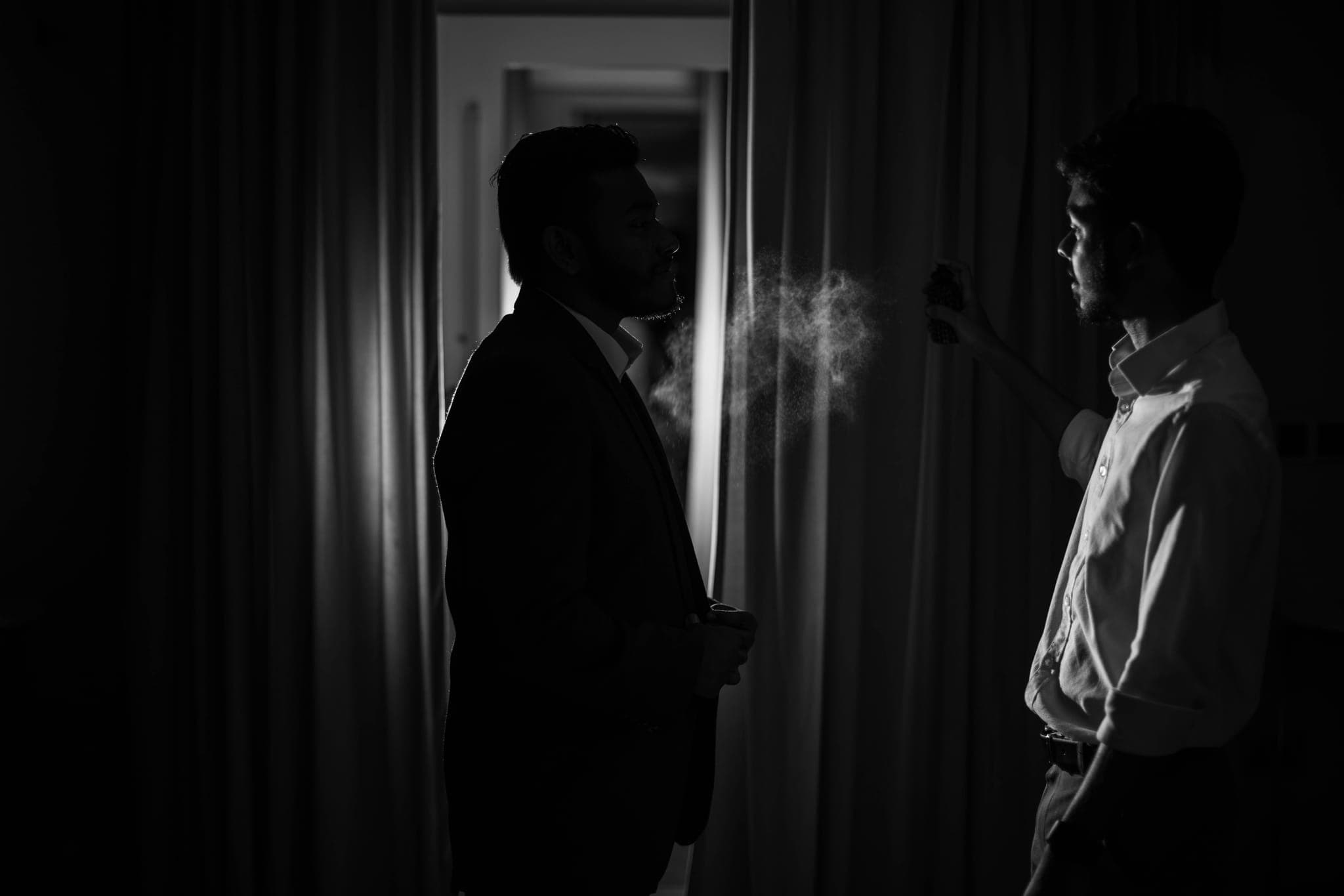 Two men silhouetted in dark curtained room with smoke