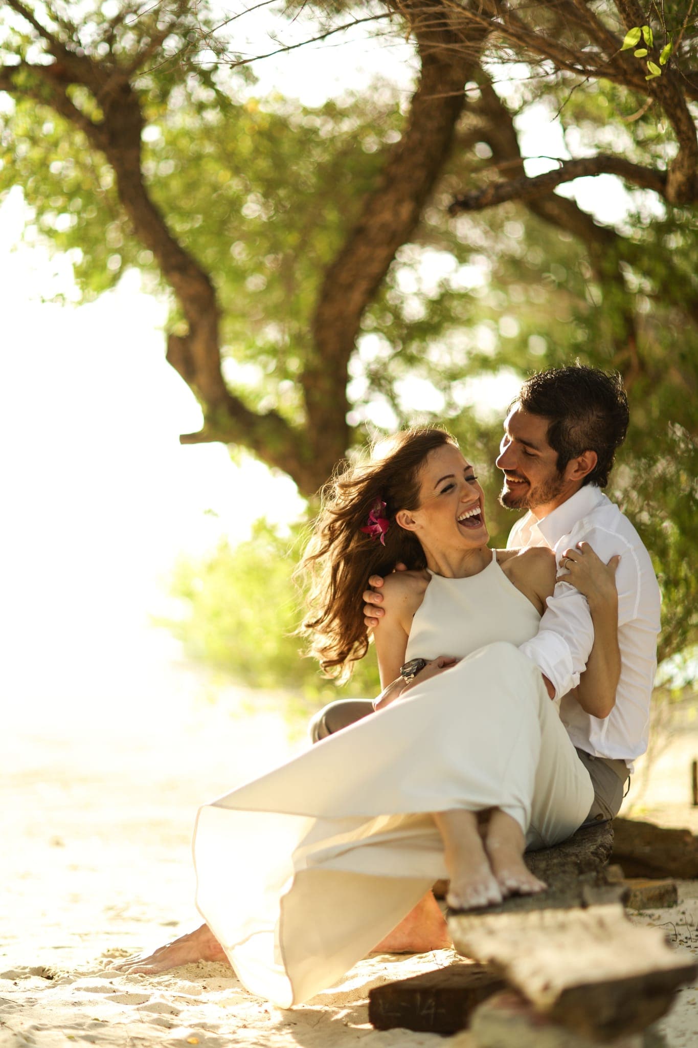 Bride and groom laughing together on sunlit beach