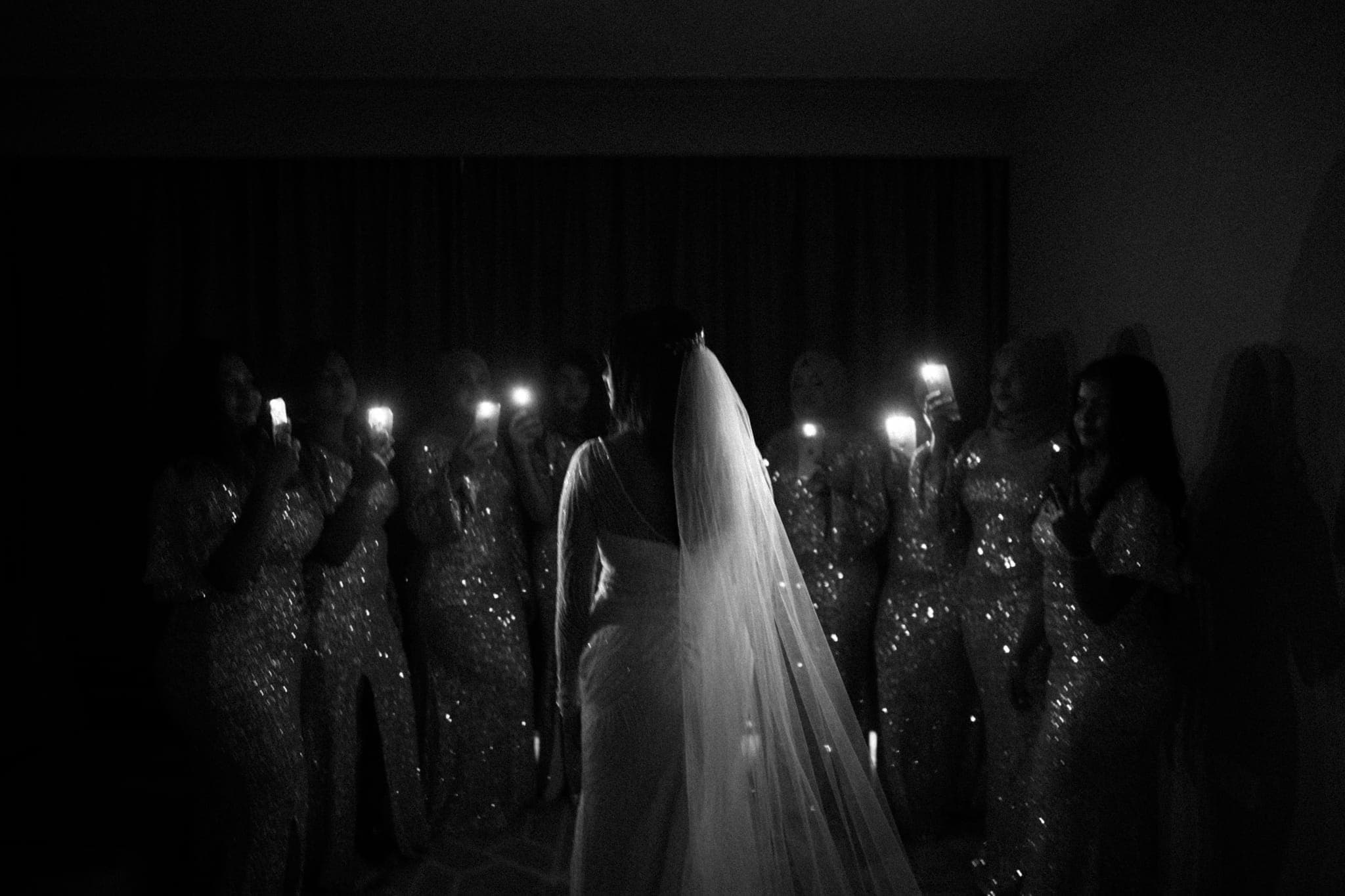 Bride walking past bridesmaids holding candles, black and white