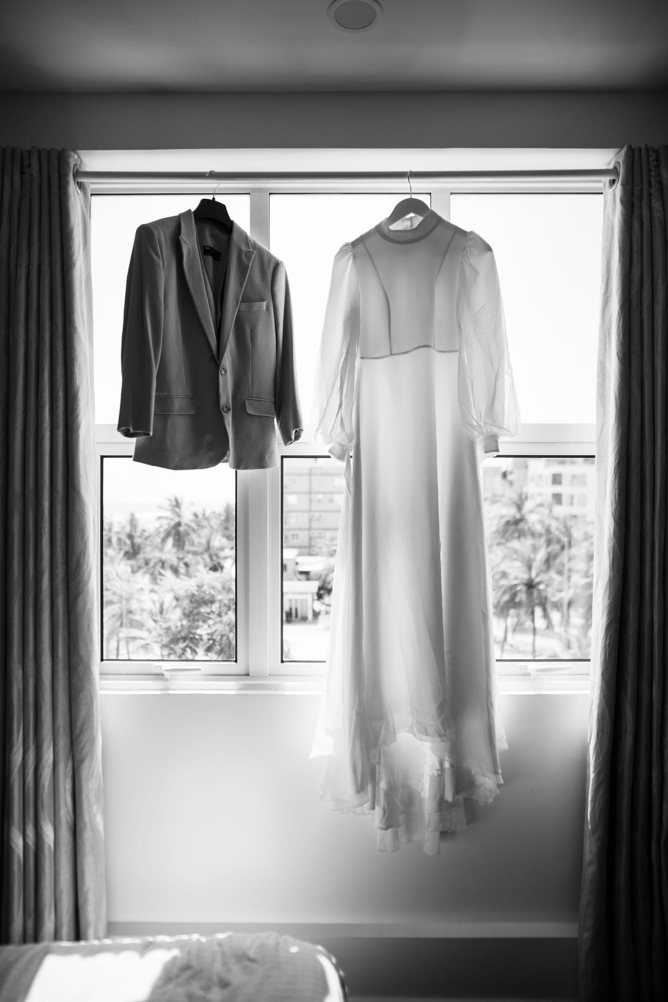 Wedding dress and suit jacket hanging in window light