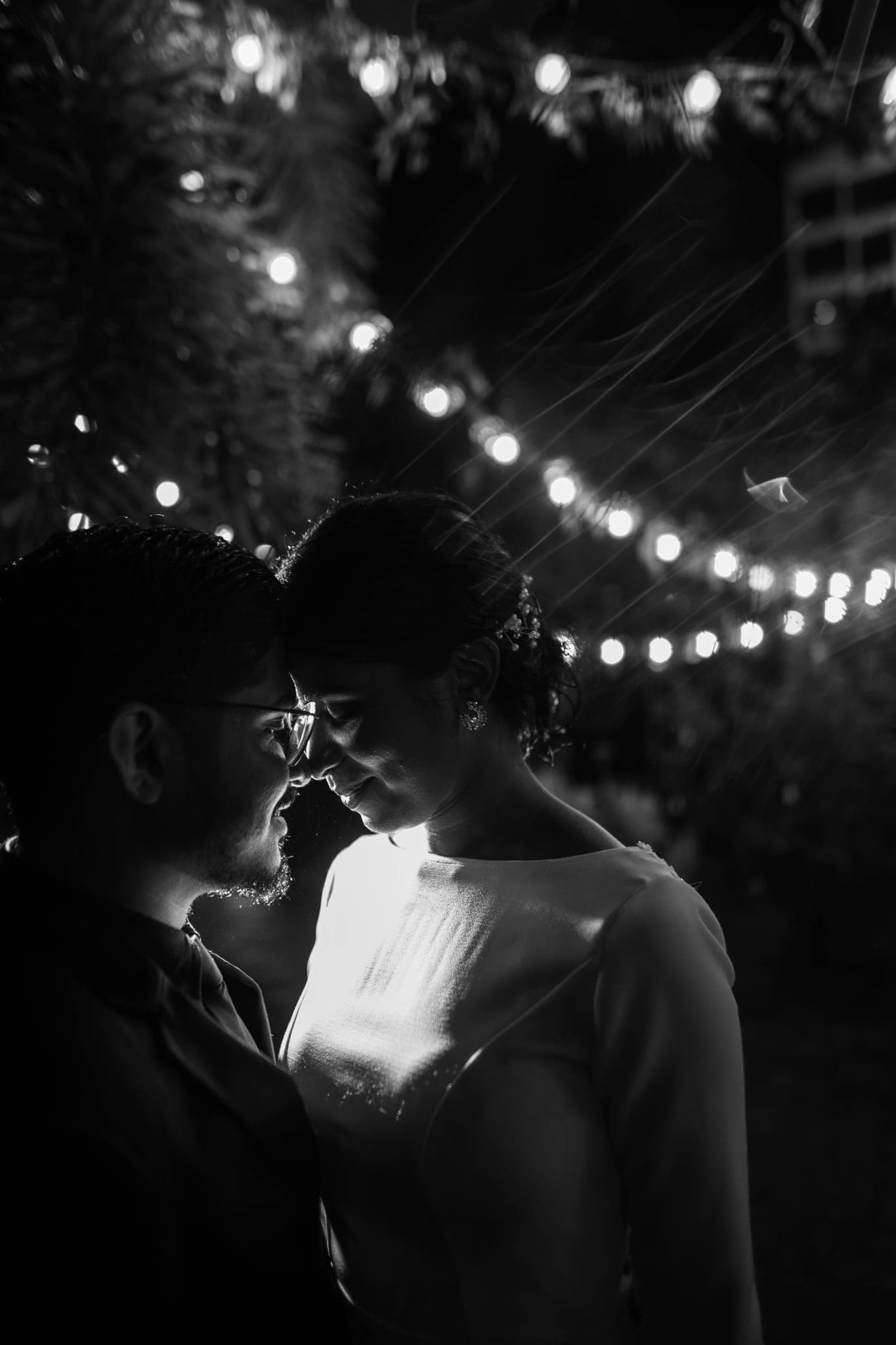 Couple embracing under string lights at night, silhouette