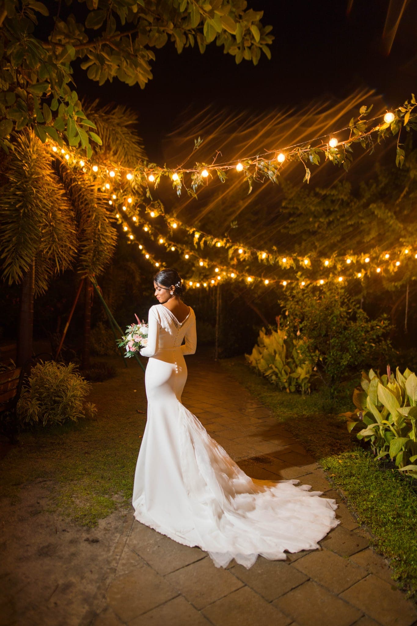 Bride in mermaid gown standing beneath fairy lights