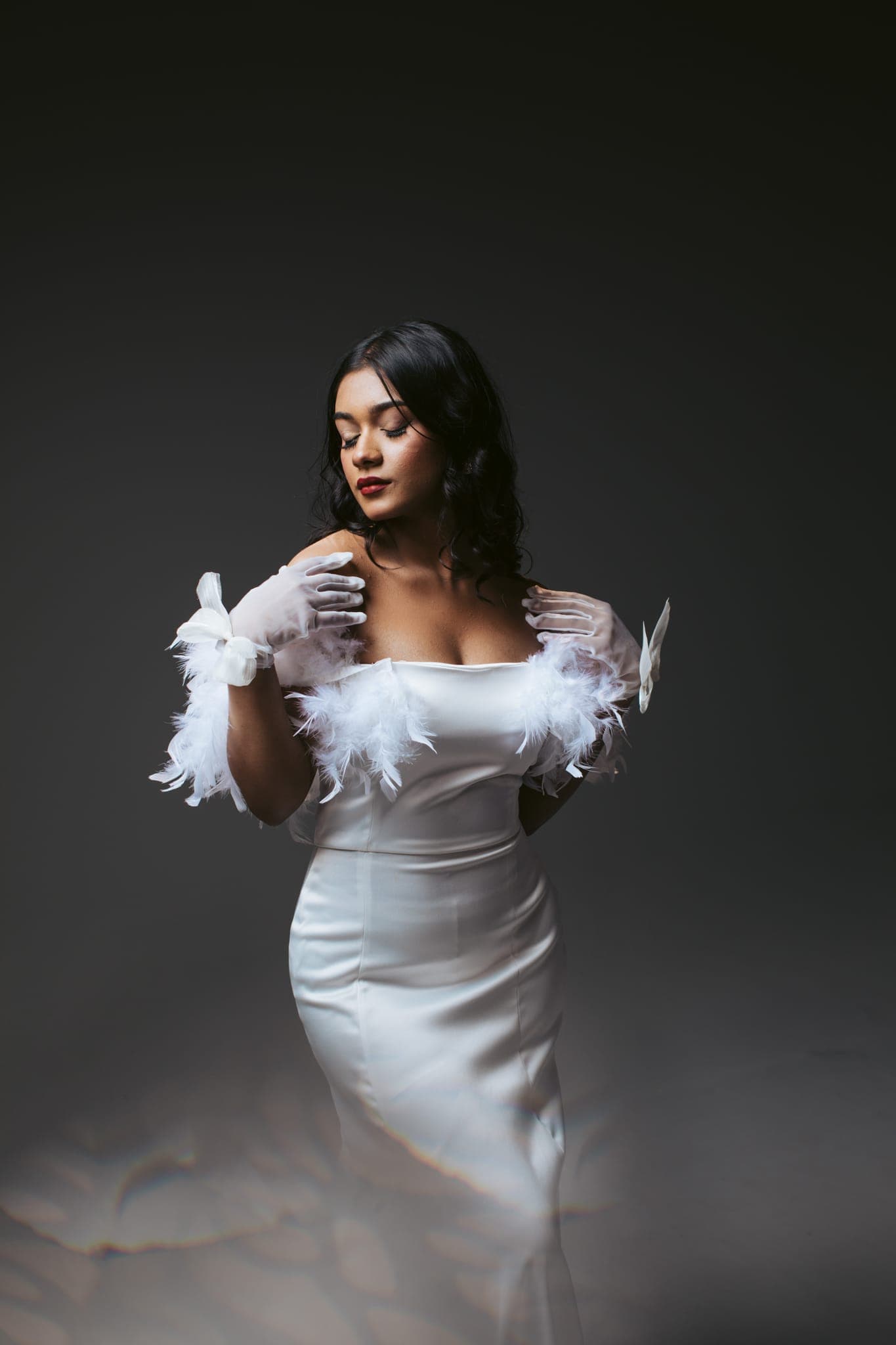 Bride in white gown and gloves against dark studio backdrop