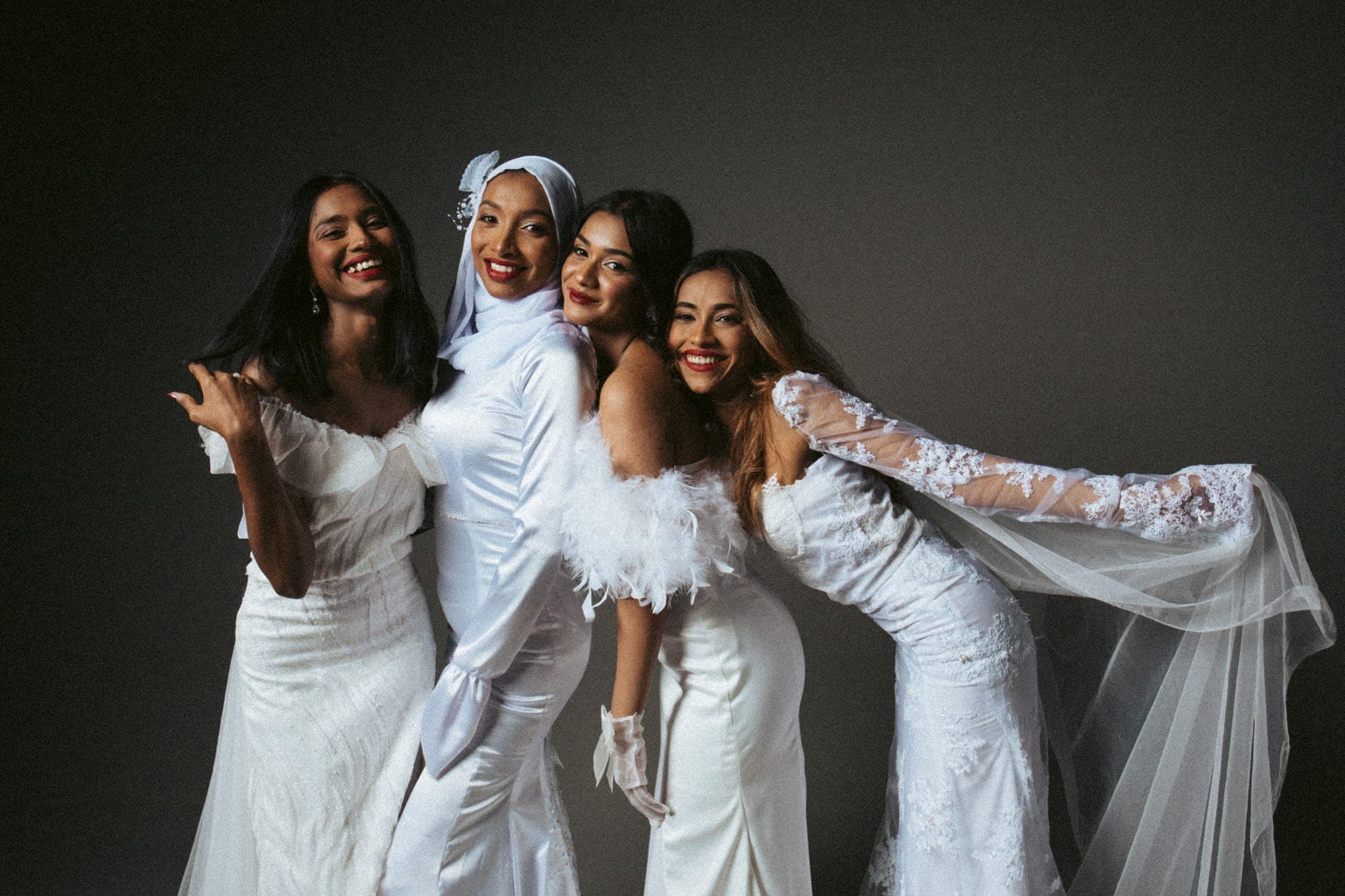 Four women in white bridal-style gowns laughing together