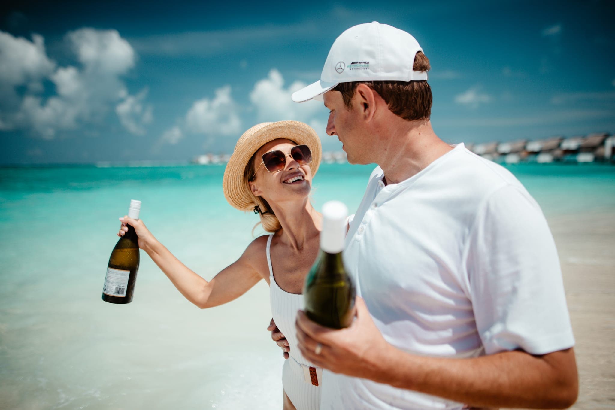 Couple toasting with wine bottles on tropical beach
