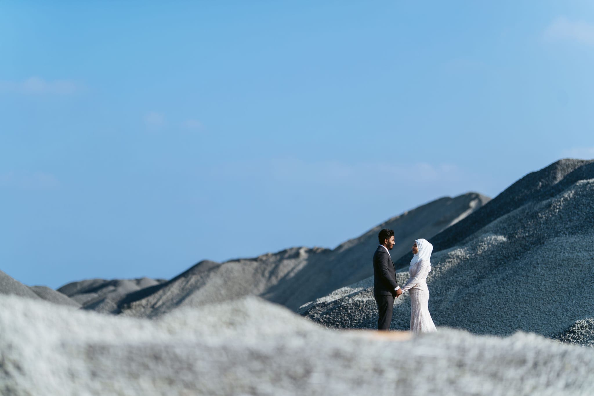 Bride and groom standing tiny amid sand dune landscape