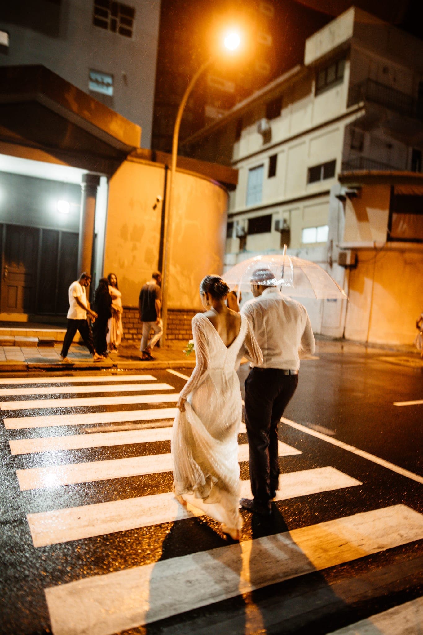 Bride and groom crossing crosswalk at night in rain