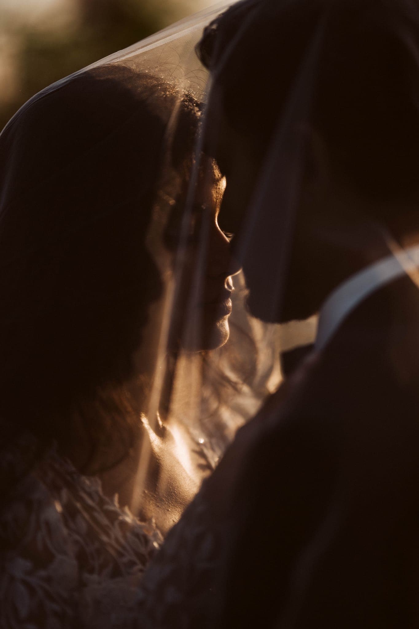 Bride and groom nearly kissing beneath sunlit veil
