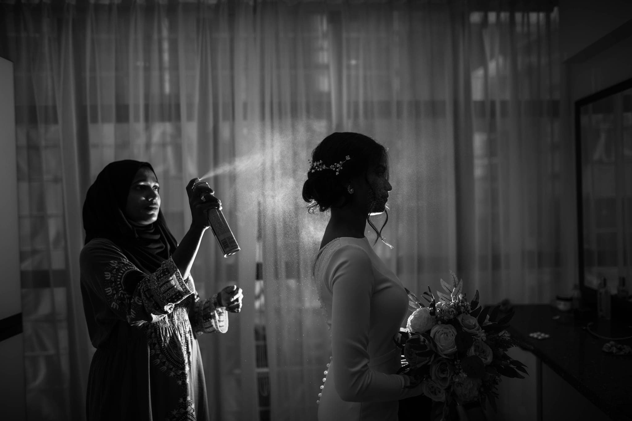 Bride having hair sprayed while holding bouquet