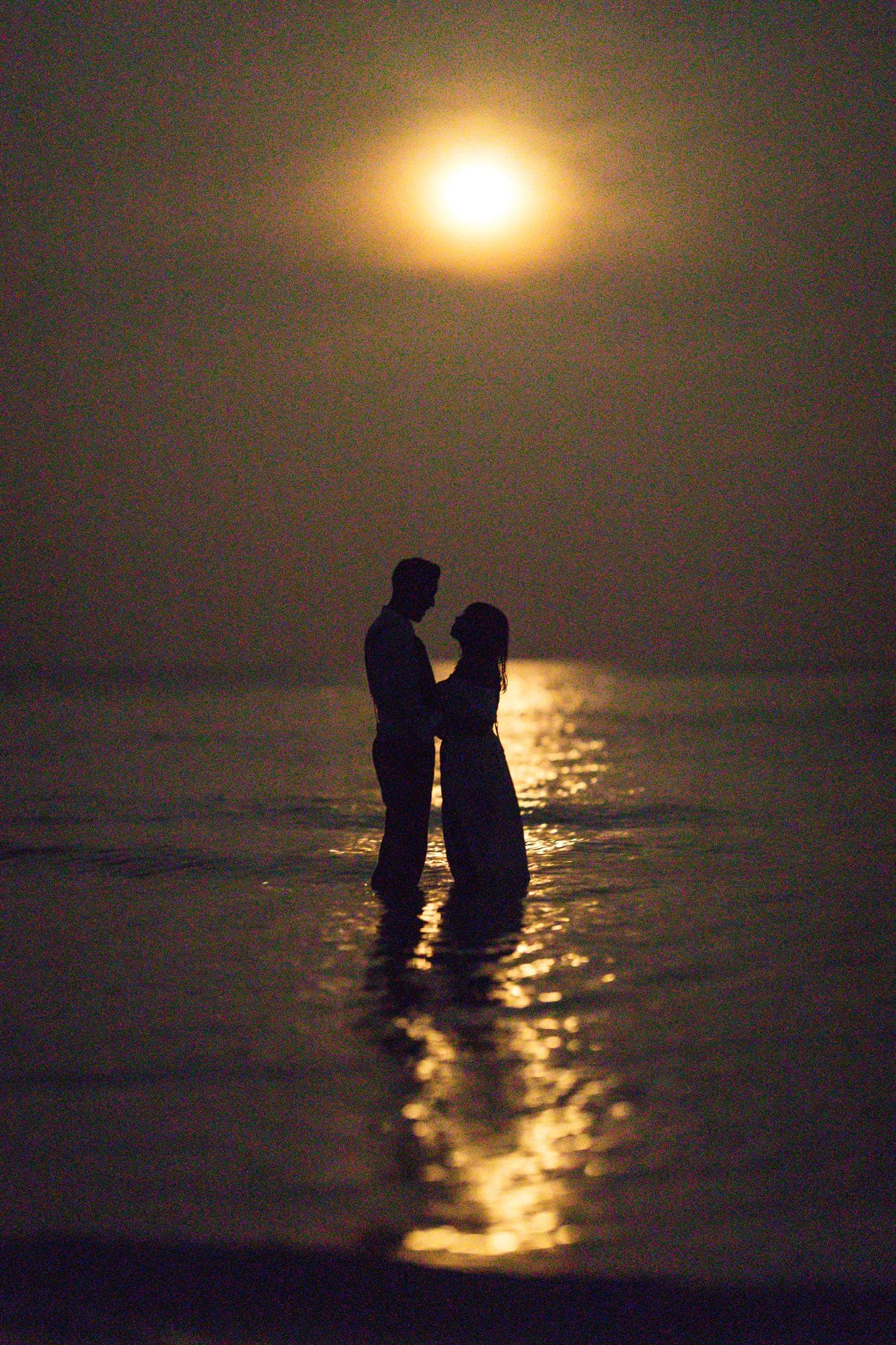 Couple embracing in sea with full moon glow