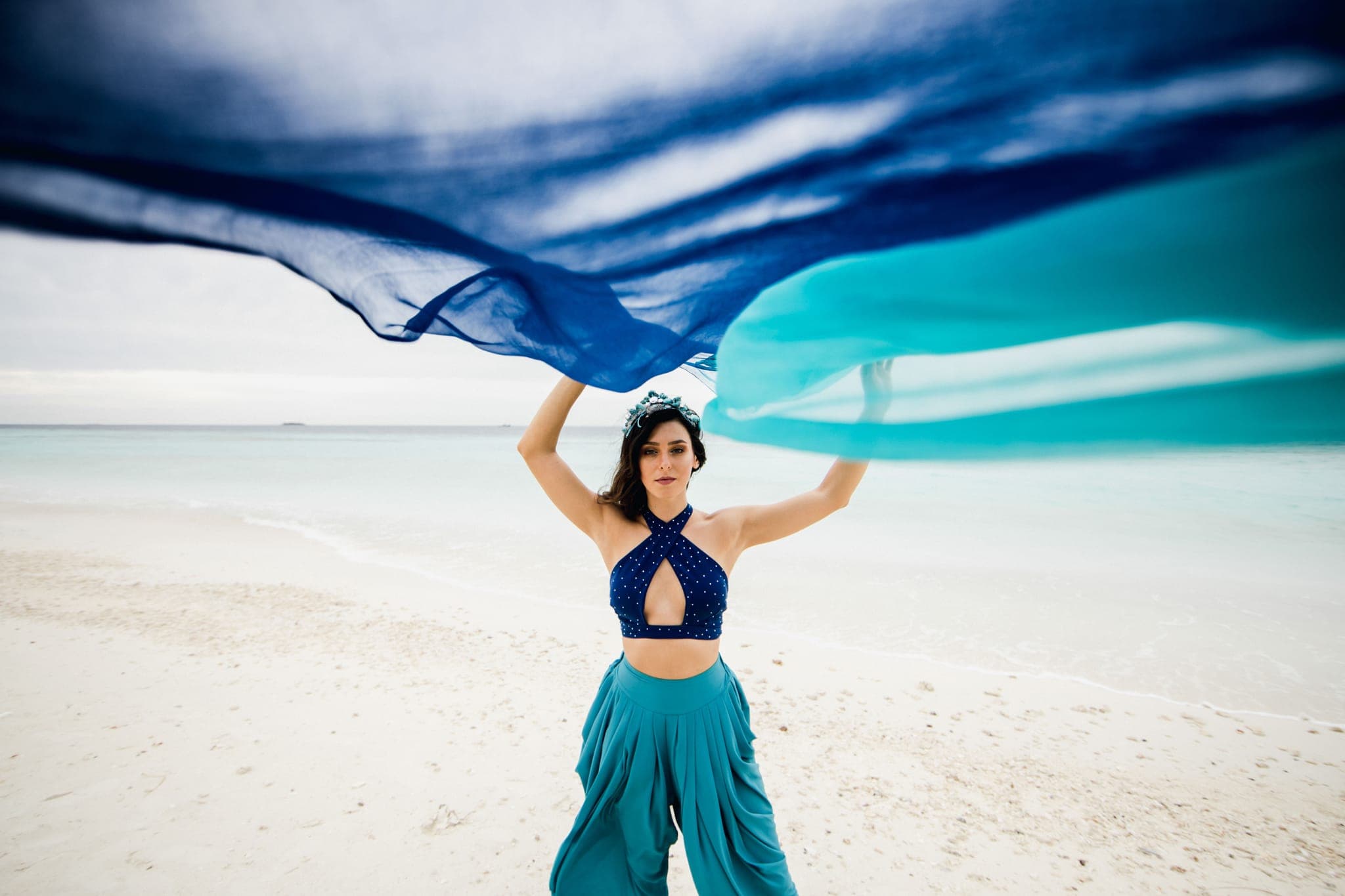 Woman in blue gown twirling flowing scarf on beach
