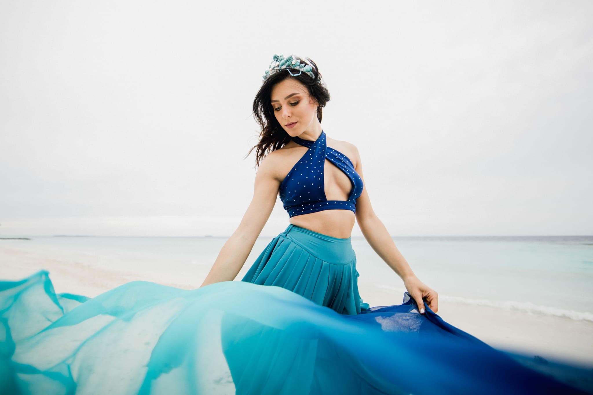 Woman in teal gown with tiara on sandy beach