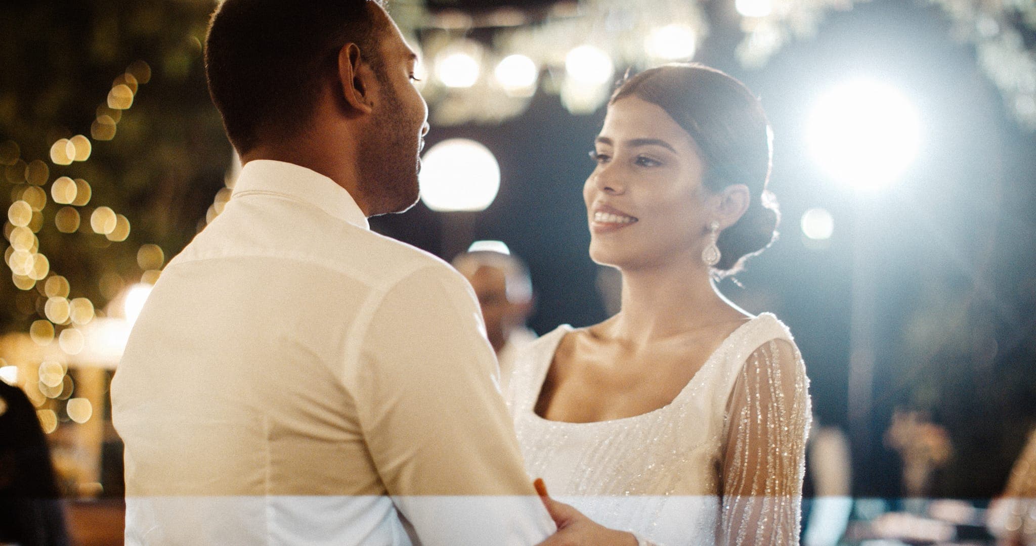 Bride and groom smiling at night among string lights
