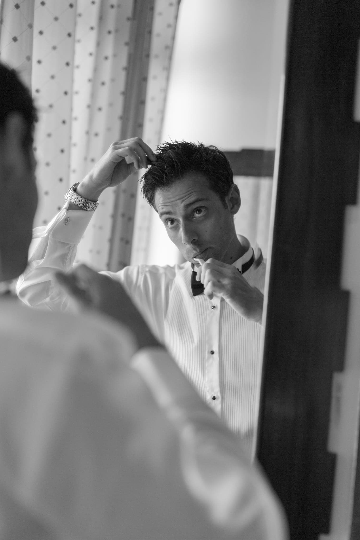 Groom fixing hair in mirror, black and white