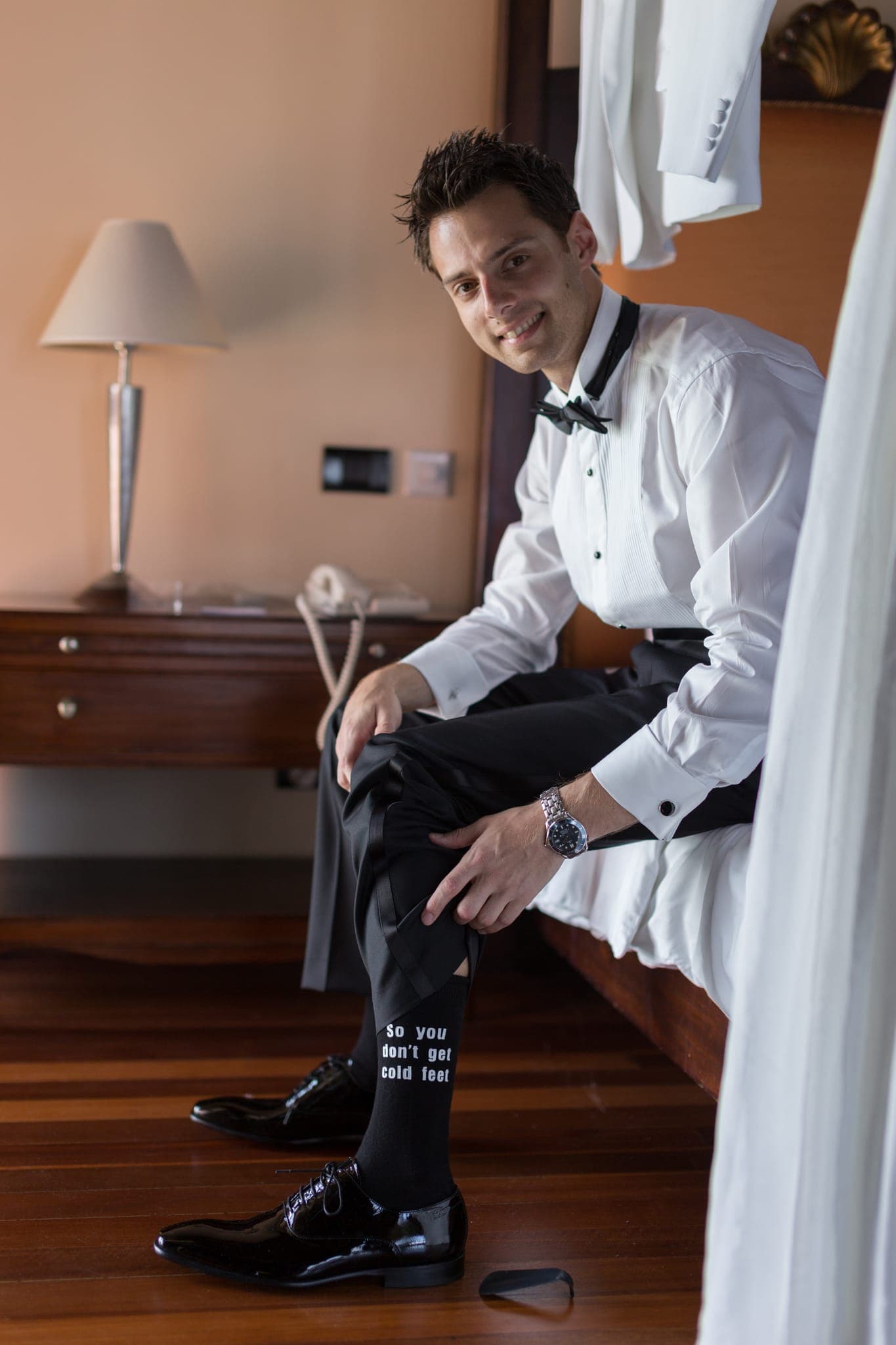 Groom seated putting on shoes in hotel room