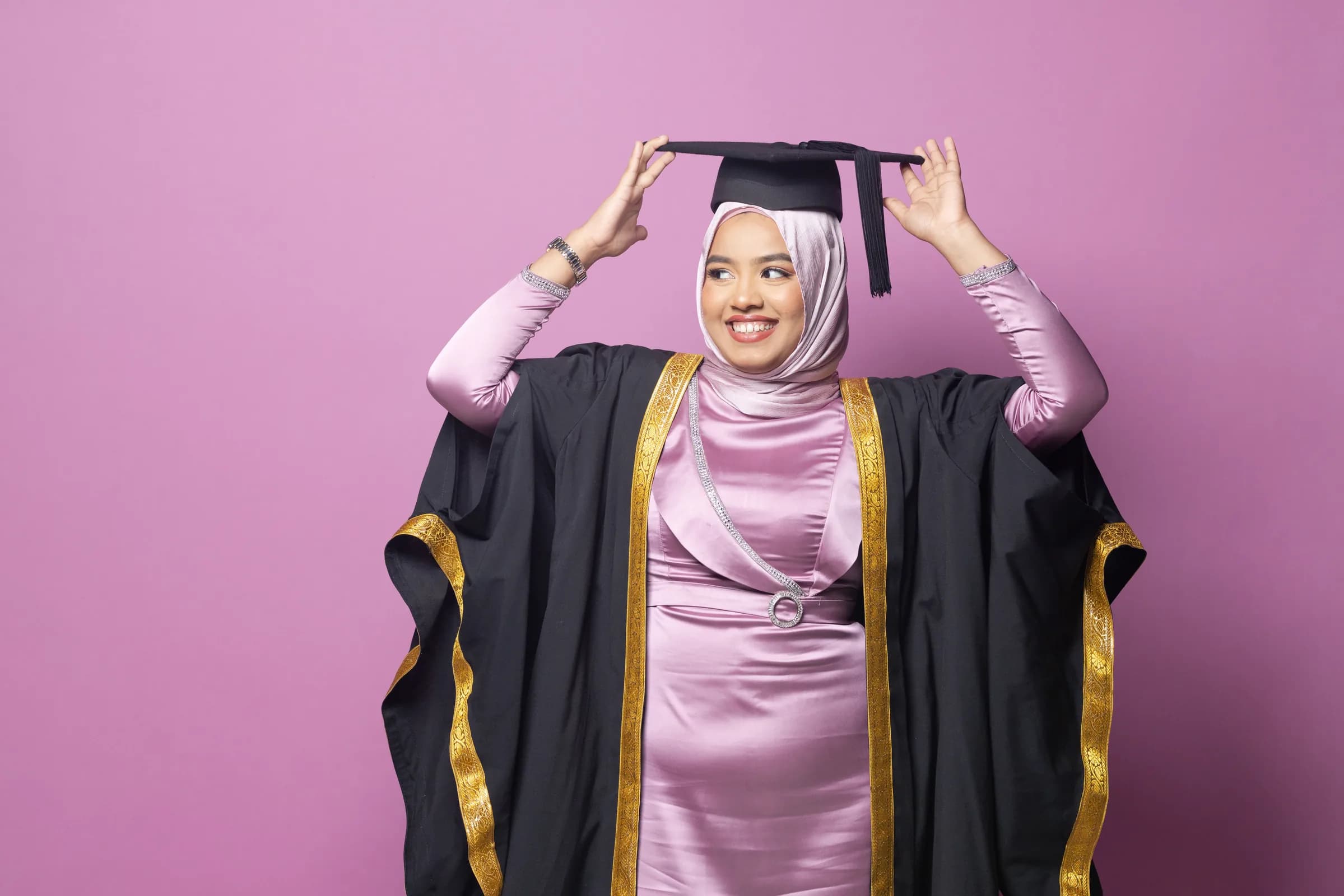 Graduate in a cap and gown against a pink backdrop