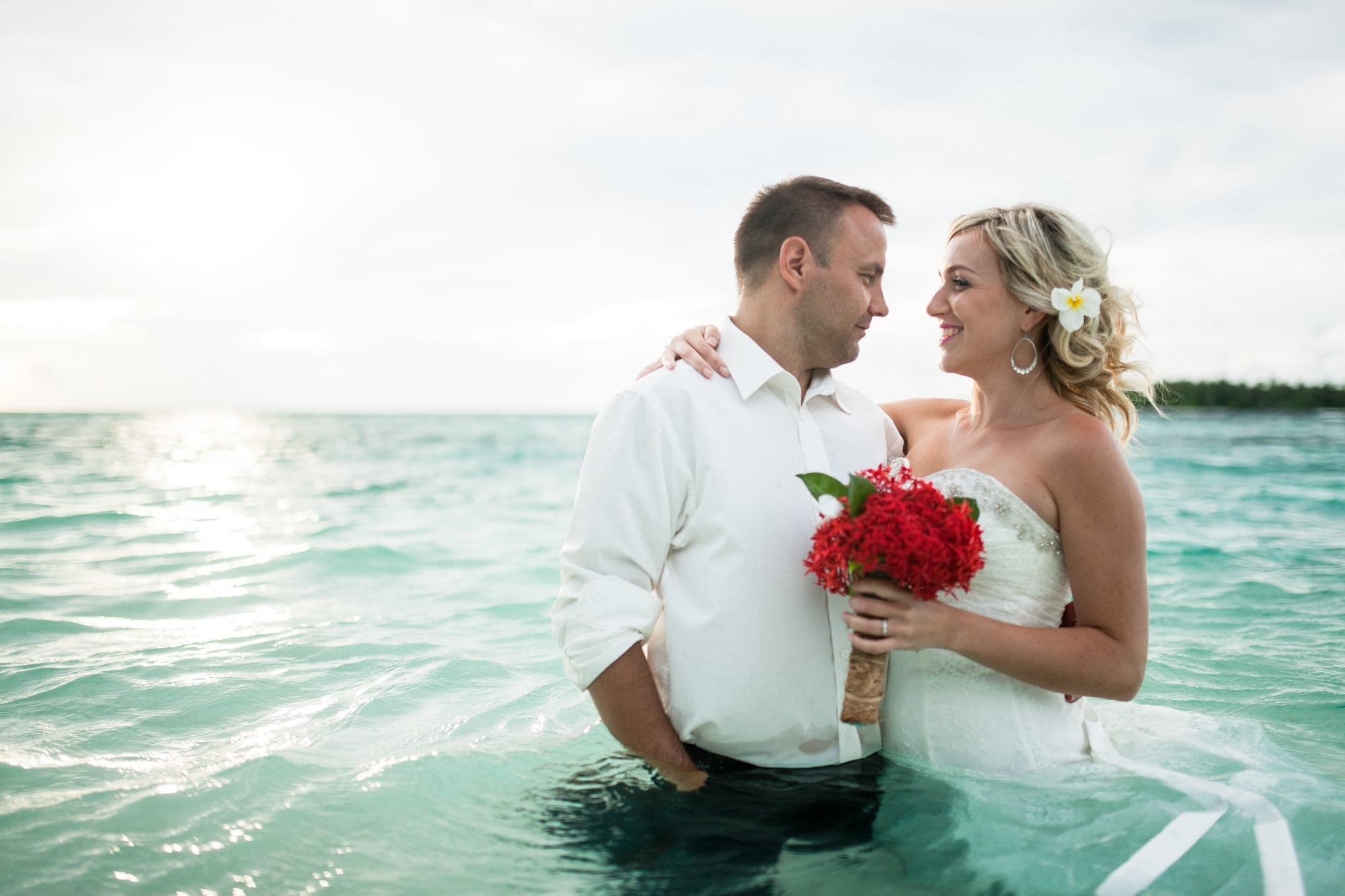 Bride and groom embracing waist-deep in turquoise water