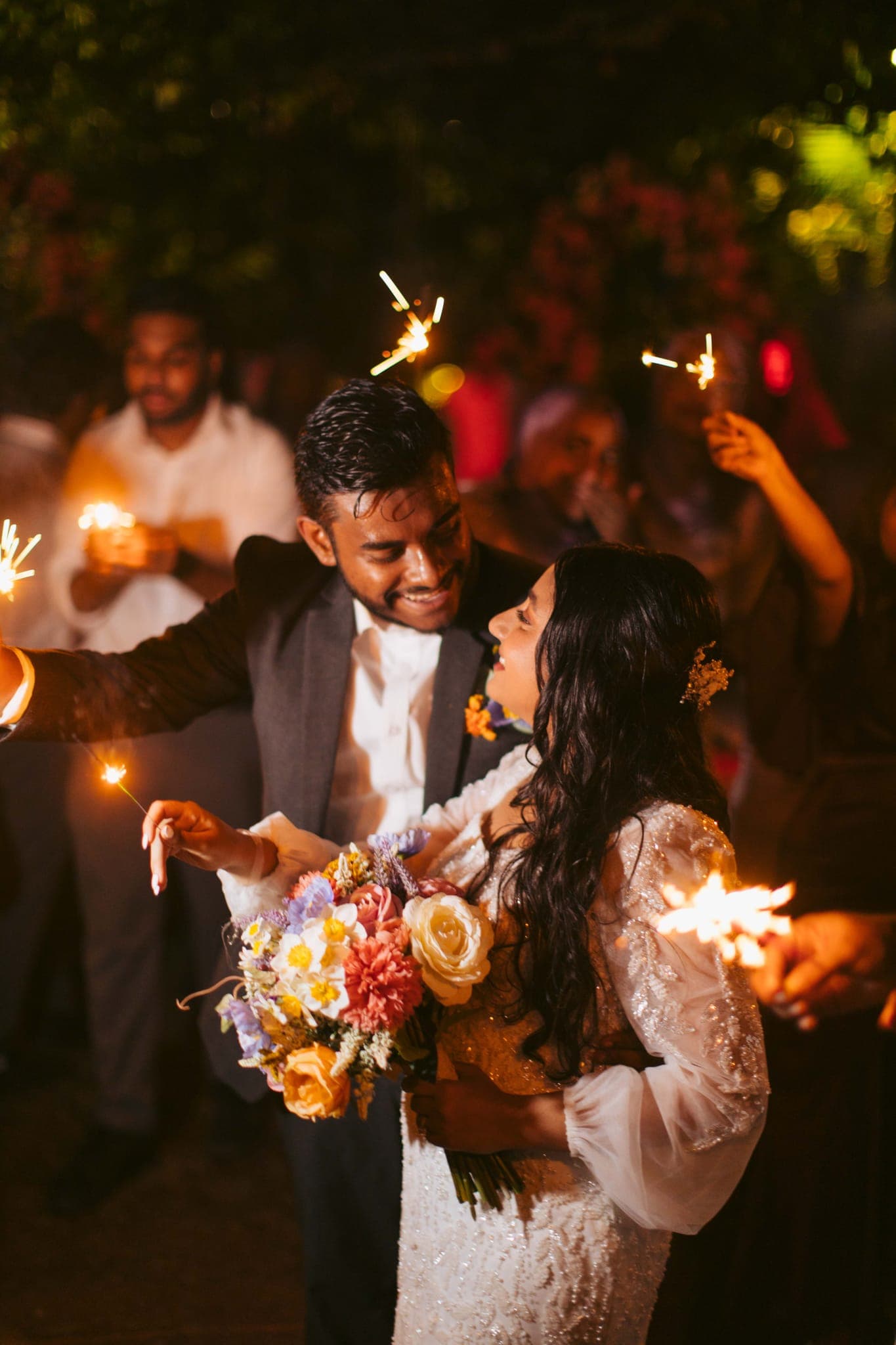 Bride and groom holding sparklers with flowers at night