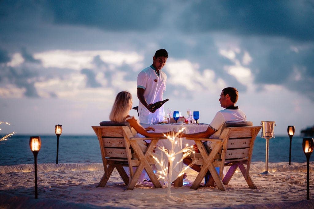 Waiter serving couple at romantic candlelit beach dinner