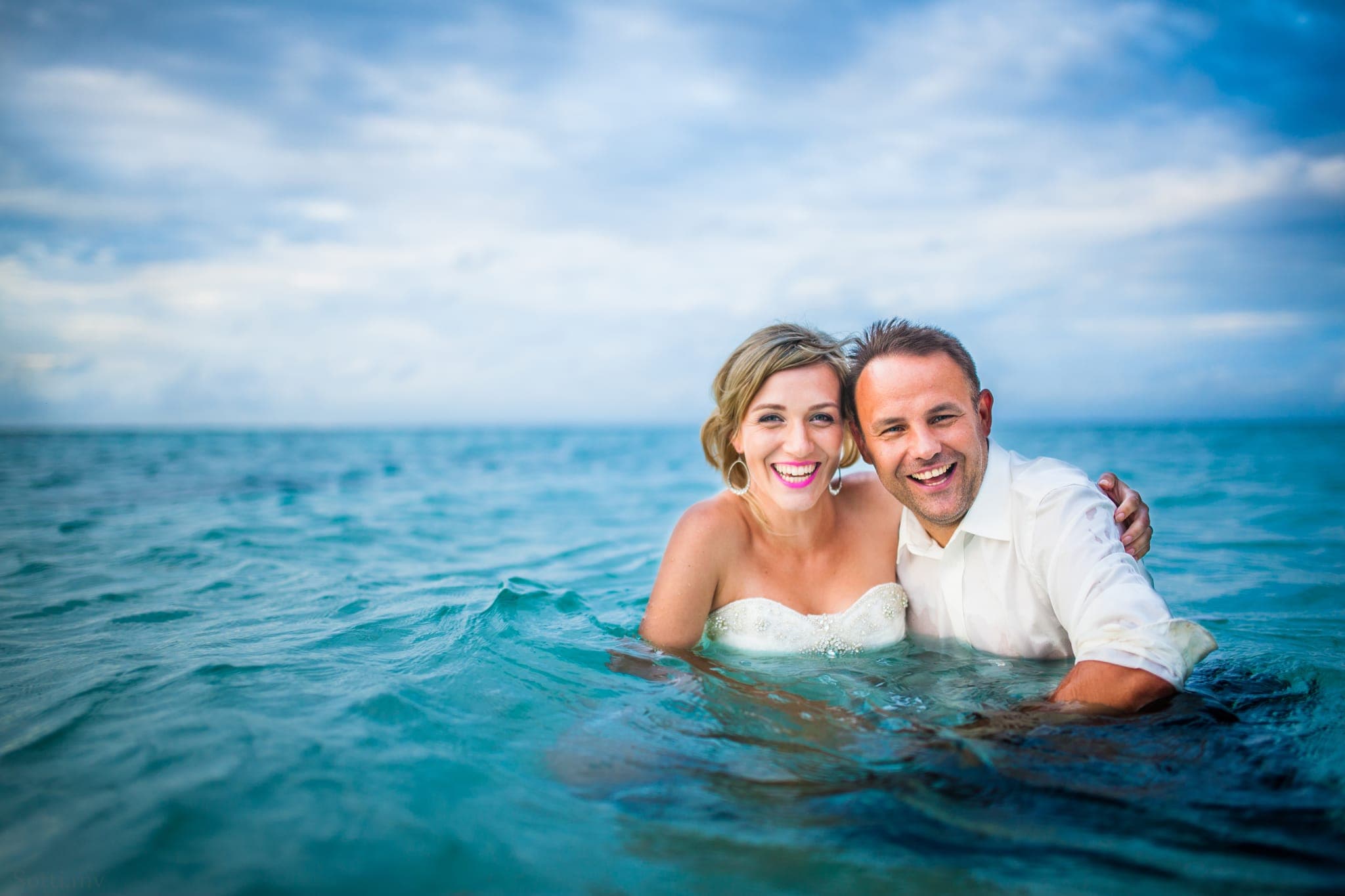 Bride and groom smiling while standing in turquoise ocean